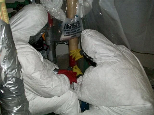 Techniciens en combinaison de protection traitant une canalisation calorifugée à l'amiante (photo d'illustration)